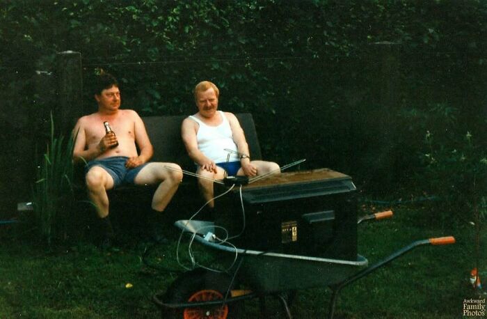Two men in casual summer clothes sitting awkwardly outside, sharing a relaxed moment in an awkward family photo. Two men in casual summer clothes sitting awkwardly outside, sharing a relaxed moment in an awkward family photo.