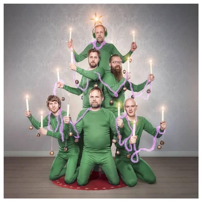 Six men dressed as a human Christmas tree, holding candles and wearing green outfits, creating a funny Christmas card.