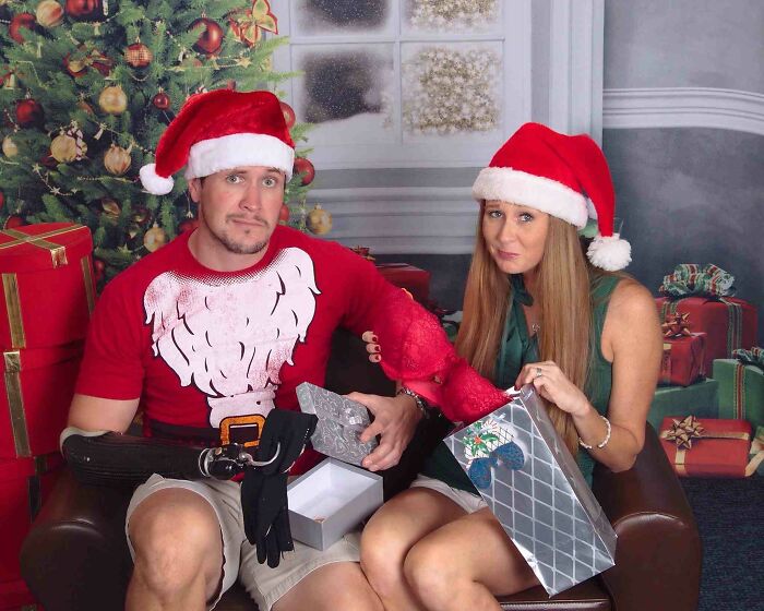 A couple in Santa hats holding funny Christmas cards, surrounded by gifts, creating laughter.