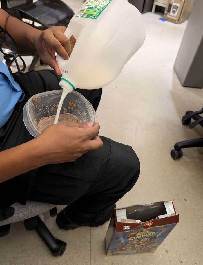 A coworker humorously pours milk into a cereal bowl in the office.