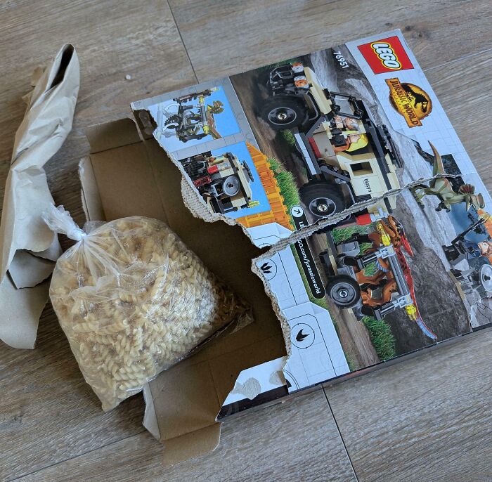Torn LEGO Jurassic World box with a bag of pasta inside, illustrating careless online shopping backfired in a funny way.