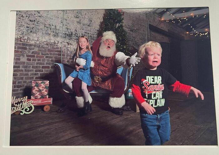 Funny Christmas card with Santa, a happy girl on his lap, and a crying boy wearing a "Dear Santa, I can explain" shirt.