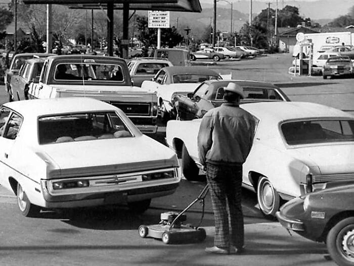 Traffic jam in 1973, depicting a man with a lawn mower amidst vintage cars. Traffic jam in 1973, depicting a man with a lawn mower amidst vintage cars.
