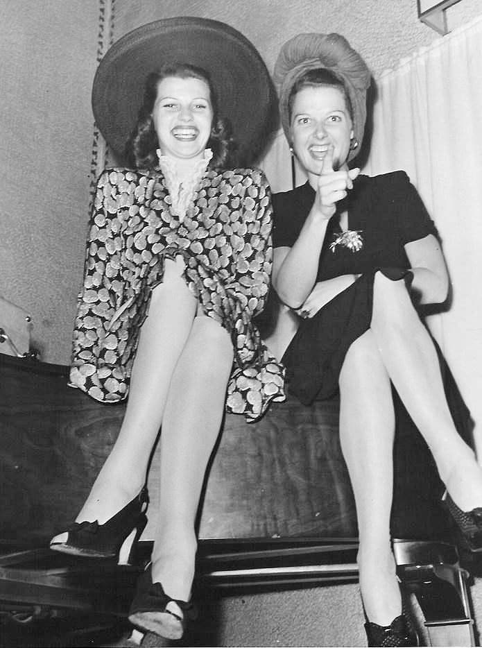 This may contain: two women sitting on top of a bed next to each other wearing hats and dresses